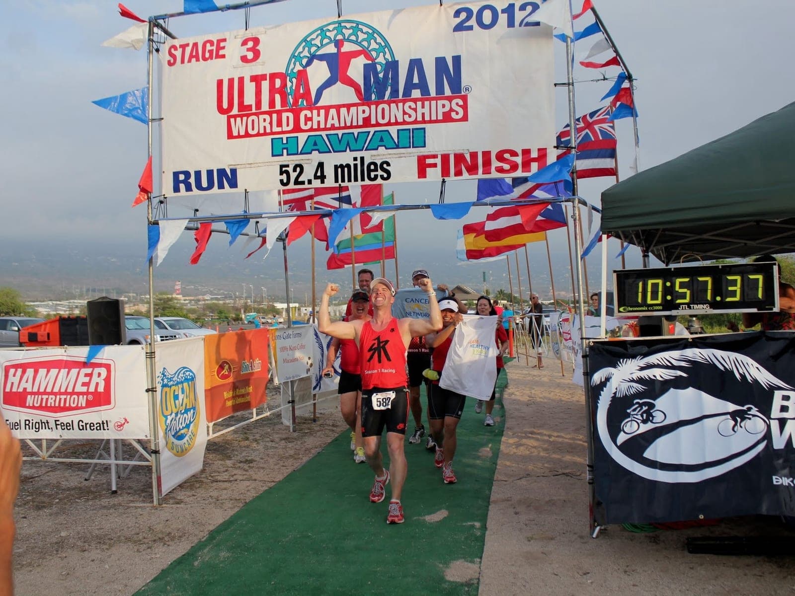 Finishing the Ultraman World Championships in Hawaii, arms raised at the line as other finishers come in behind.